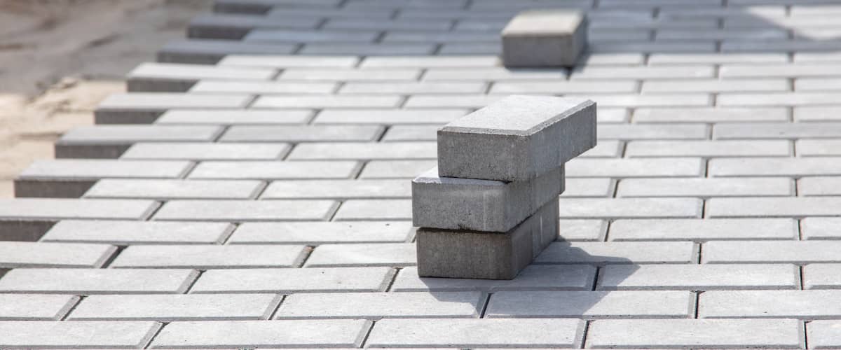 Several rectangular gray paving stones are stacked on a surface made of similar paving stones, which appear to be in the process of being installed outdoors.
